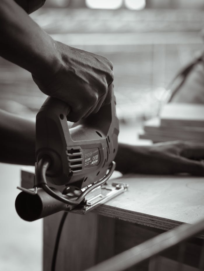 Black and white photo of a carpenter using a jigsaw to cut wood indoors, emphasizing craftsmanship.